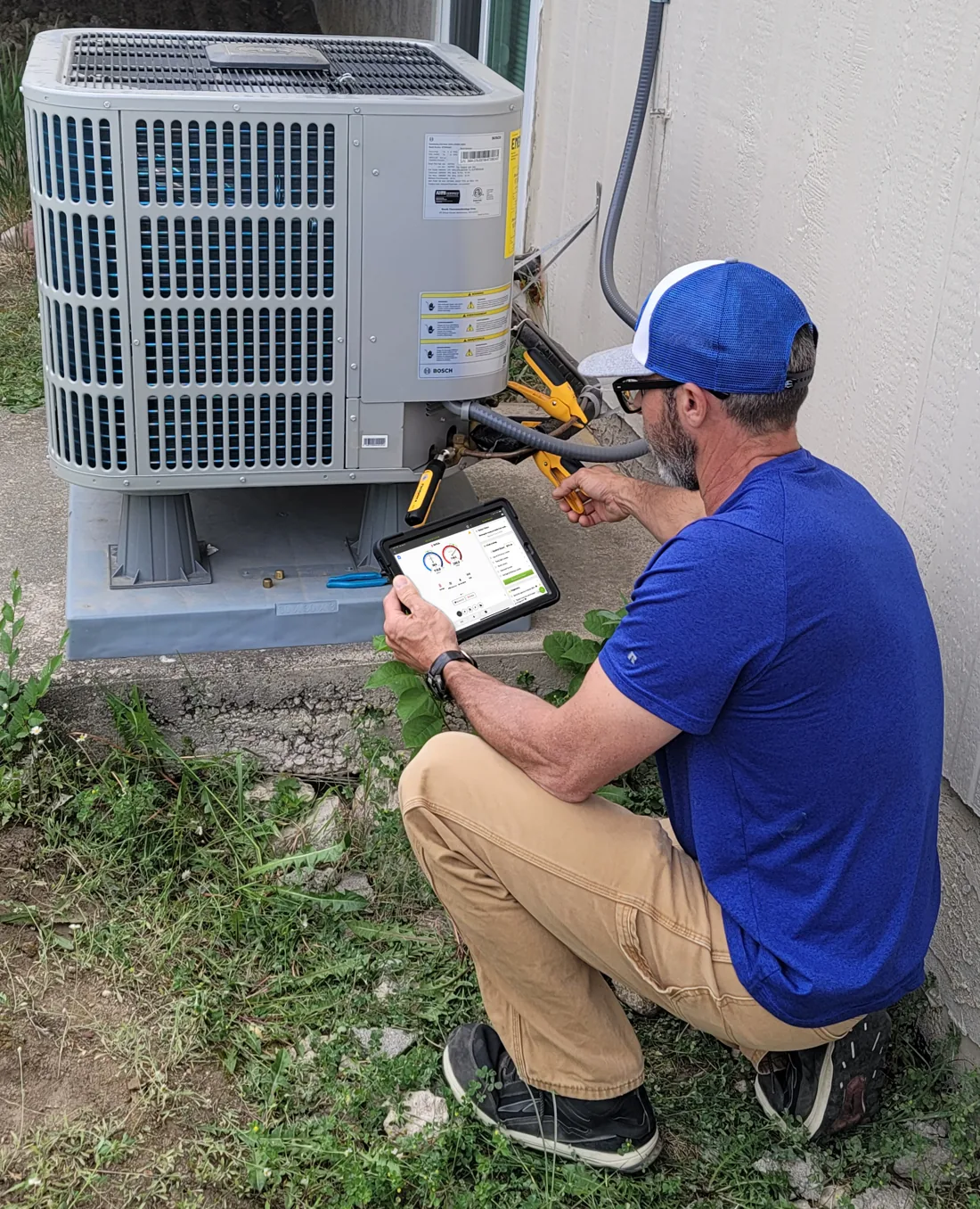 HVAC technician at an outdoor condenser running diagnostics on a tablet with the measureQuick app