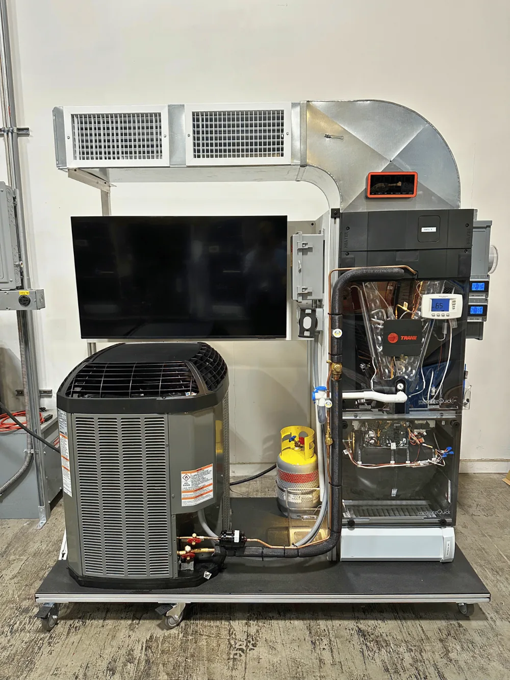 A measureQuick training unit: a fully functional HVAC system on a mobile aluminum frame with a condenser, air handler, ductwork, and a 50-inch display