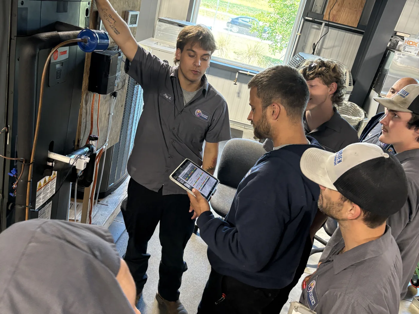 Technicians gathered around a lab air handler, reviewing live readings in the measureQuick app on a tablet during training