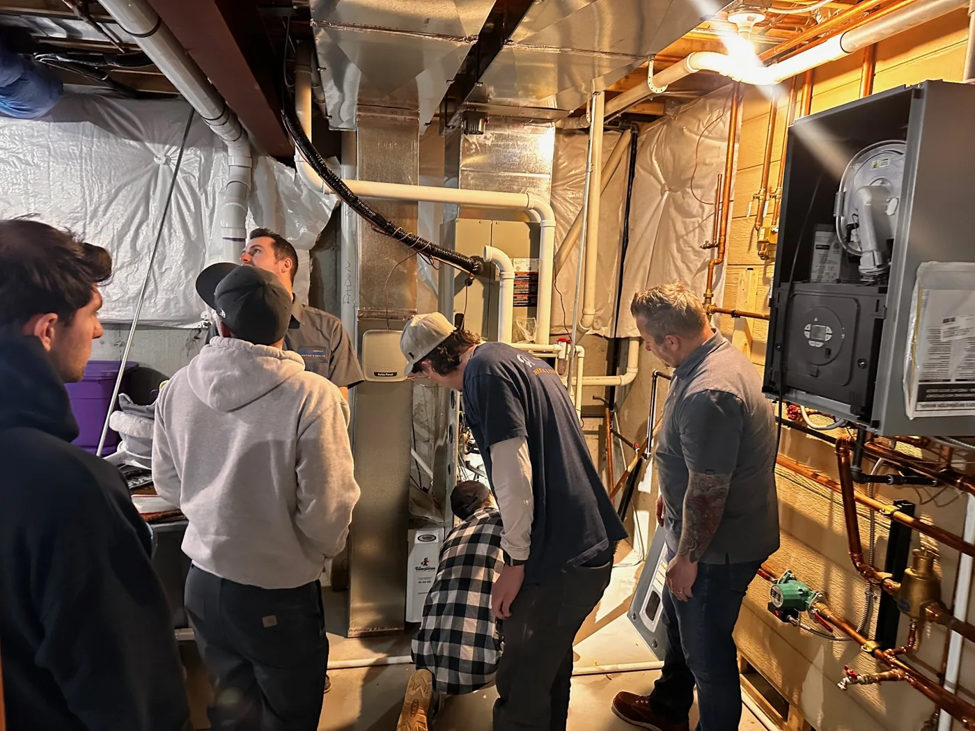 A group of technicians gathered around a residential furnace during a hands-on field training session