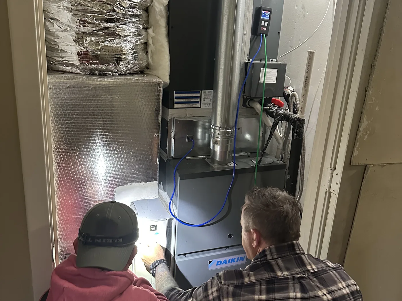 A trainer and technician measuring static pressure on a furnace with a digital manometer during hands-on training